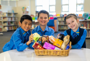 Three students smile at the camera as they show off a lovely Christmas hamper they have made